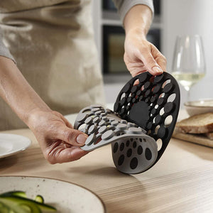 Person holding a black and gray silicone trivet on a kitchen counter.