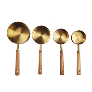 Set of four brass measuring spoons with wooden handles on a white background