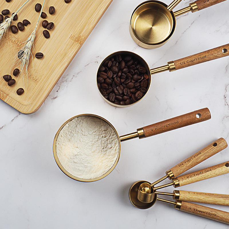 Set of measuring cups with wooden handles on a marble surface, containing different substances.