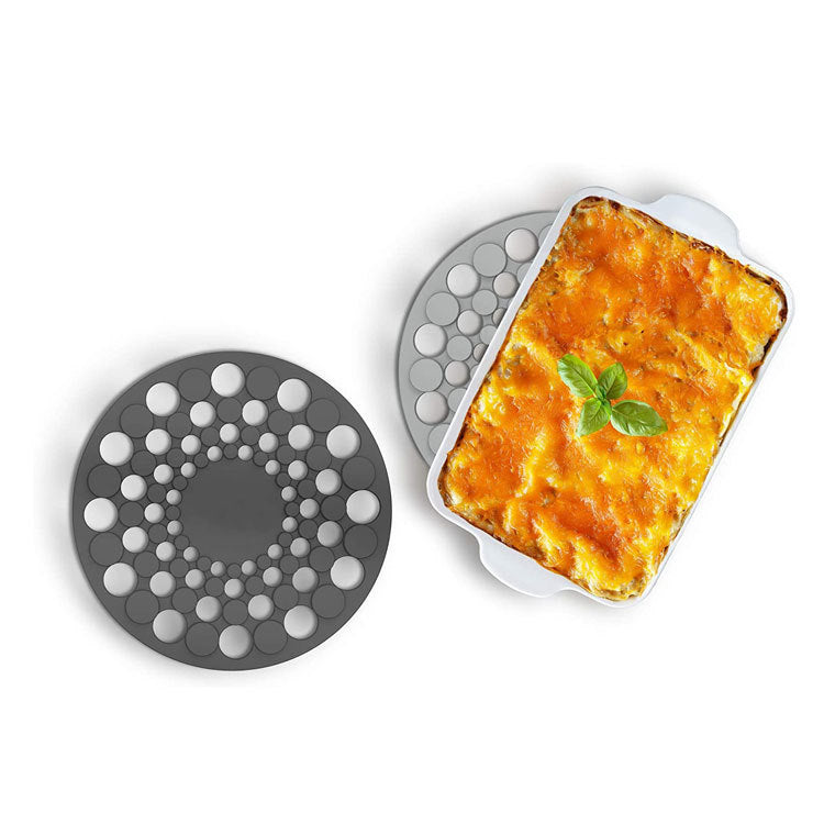 Silicone trivet with a dish of lasagna on a white background