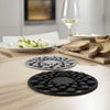 Two round silicone coasters on a wooden table with food and a glass of wine in the background.